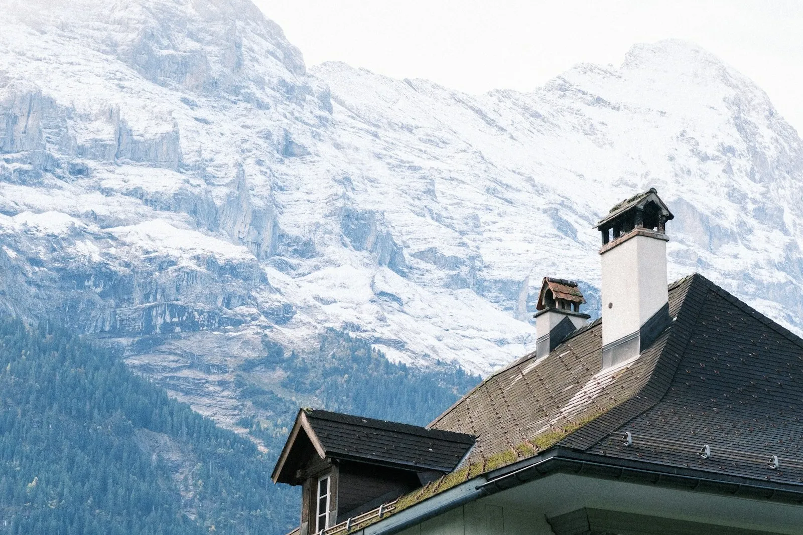 Ein Schweizer Wohnhaus mit steilem Giebeldach vor einer verschneiten Bergkette.