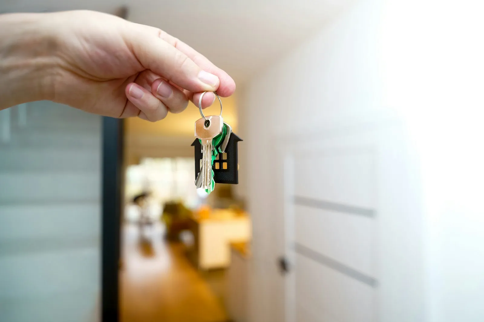 Eine Hand hält einen Wohnungsschlüssel mit Anhänger vor einer geöffneten hellen Wohnungstür.