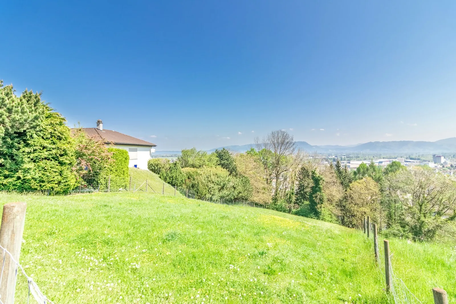 Ein weisses Einfamilienhaus am Rand einer grünen Wiese mit weiter Sicht ins Tal.