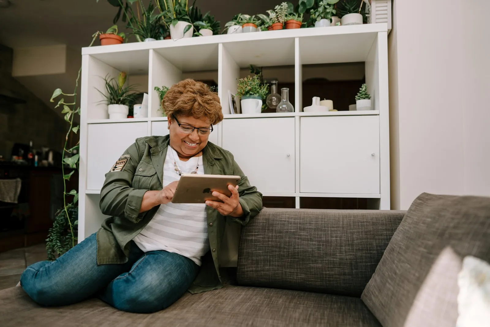 Eine ältere Frau sitzt entspannt auf dem Boden vor dem Sofa und schaut auf ein Tablet.