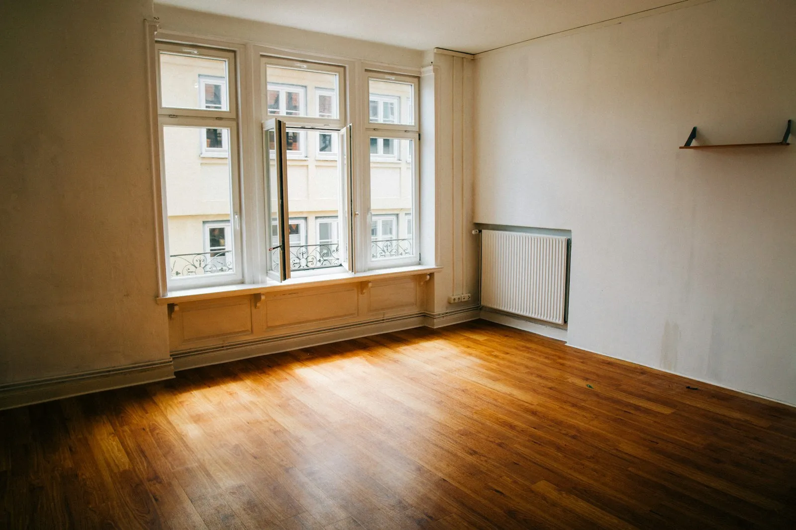 Ein leergeräumtes Zimmer mit Parkettboden, weiss gestrichenen Wänden und einem breiten Sprossenfenster.